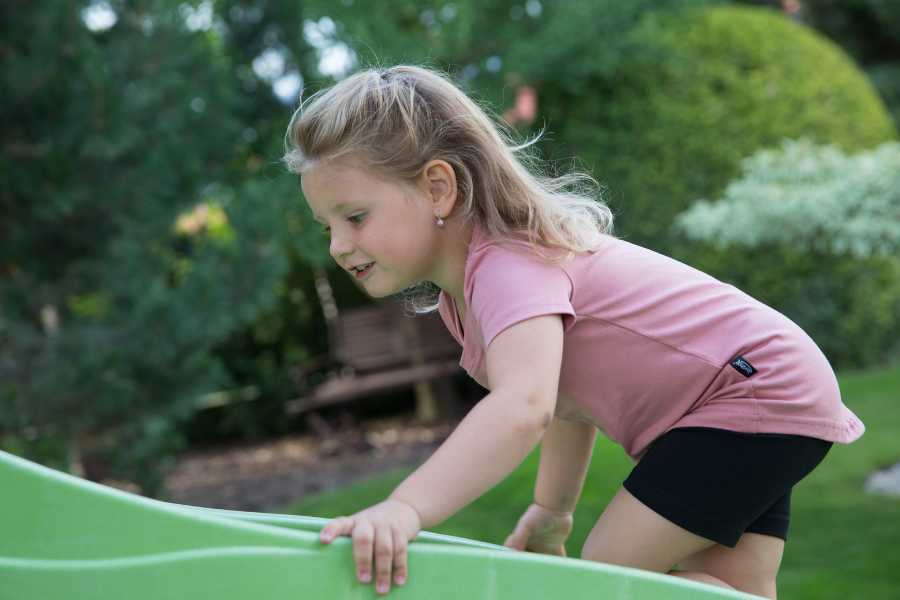 A little girl in a pink T-shirt climbs up the slide